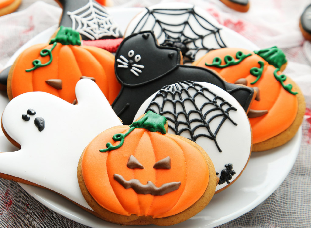 Assorted Halloween cookies decorated as pumpkins, ghosts, black cats, and spiderwebs arranged on a white plate.