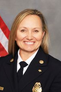 A woman with a light skin tone and blond hair wearing a military uniform and standing in front of a United States flag