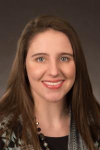 A woman with light skin tone, blue eyes, and brown hair. She is wearing a black and white sweater 