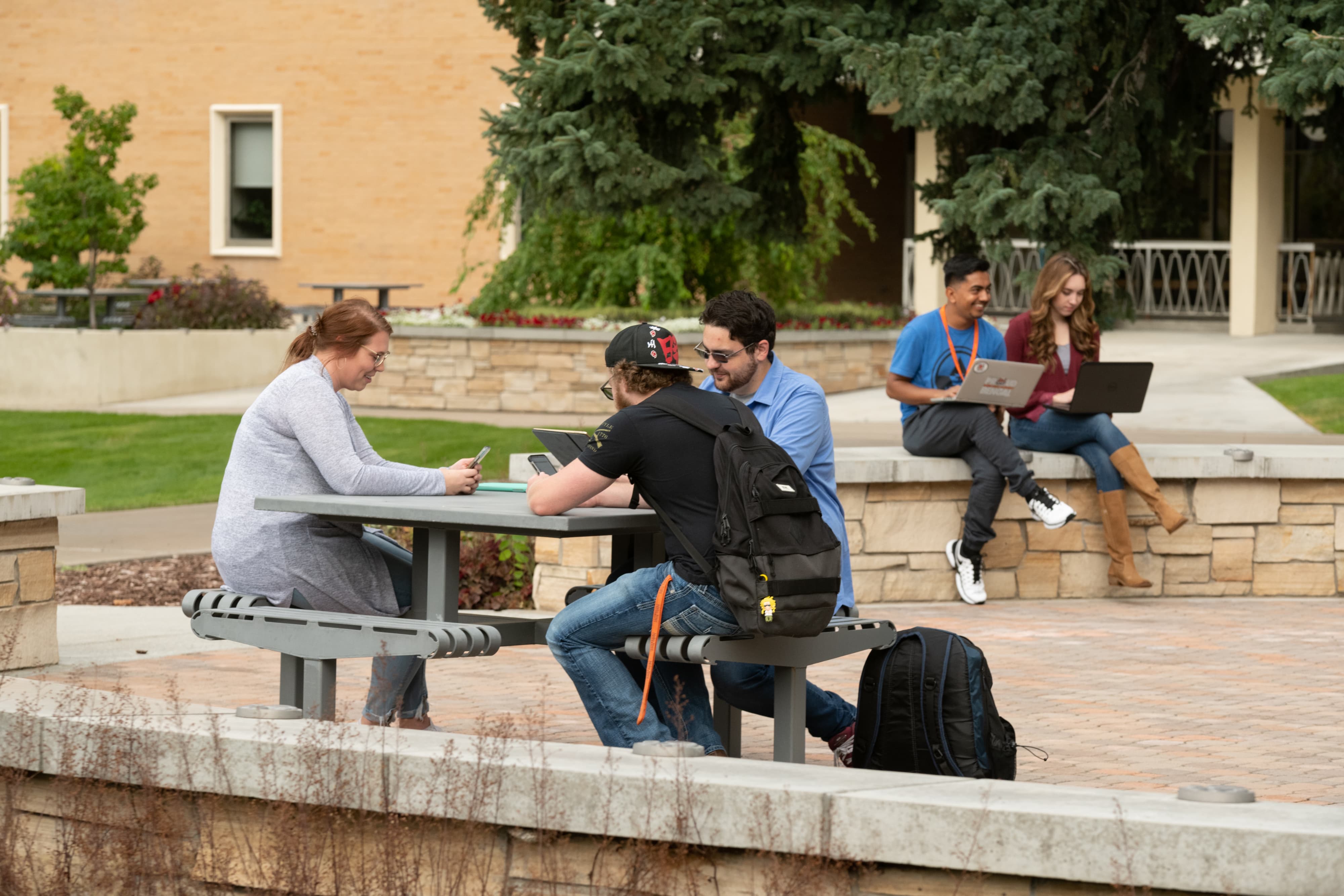 Two groups of students in an outdoor common area using technology.