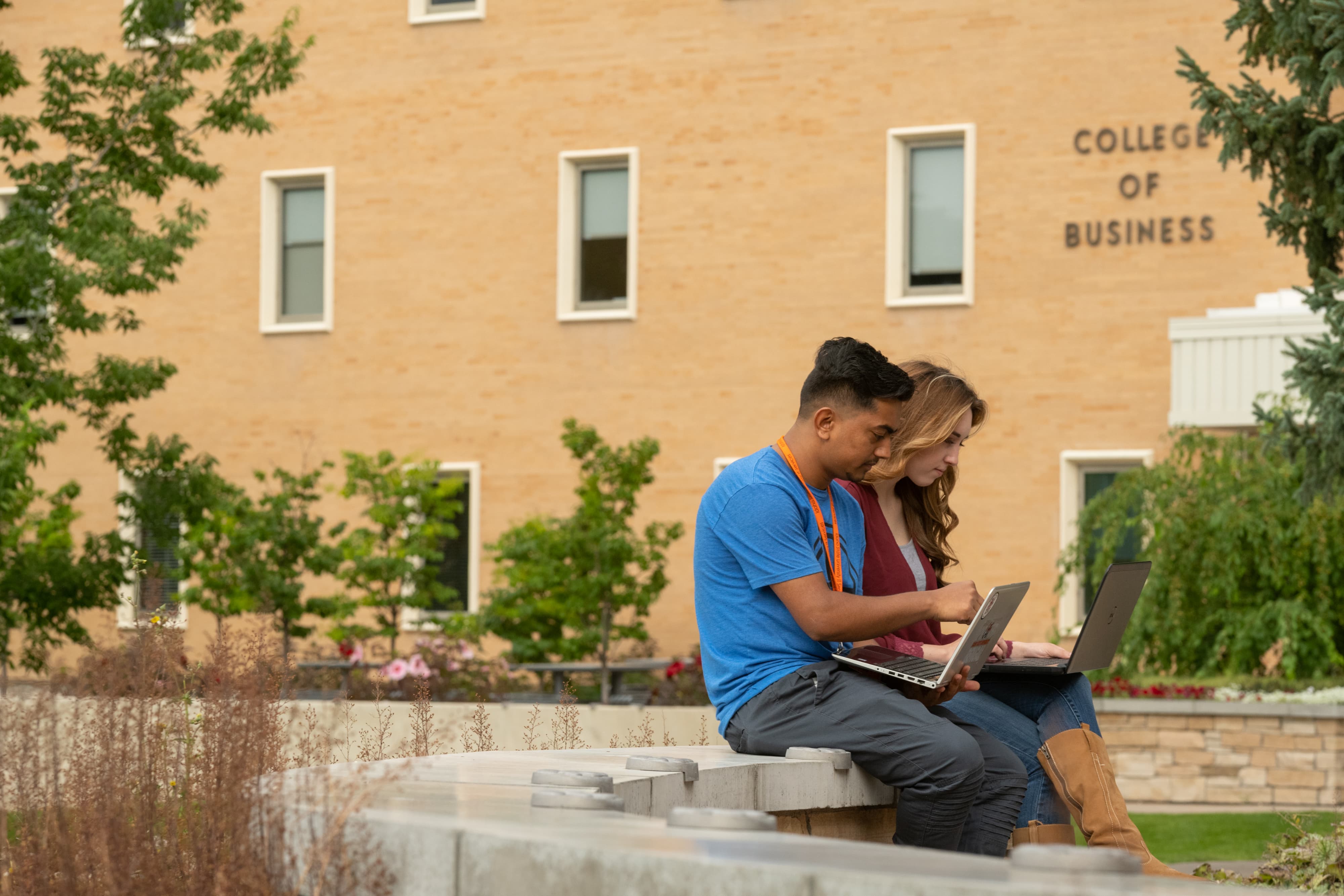 Two students sitting together outside, each with a laptop.