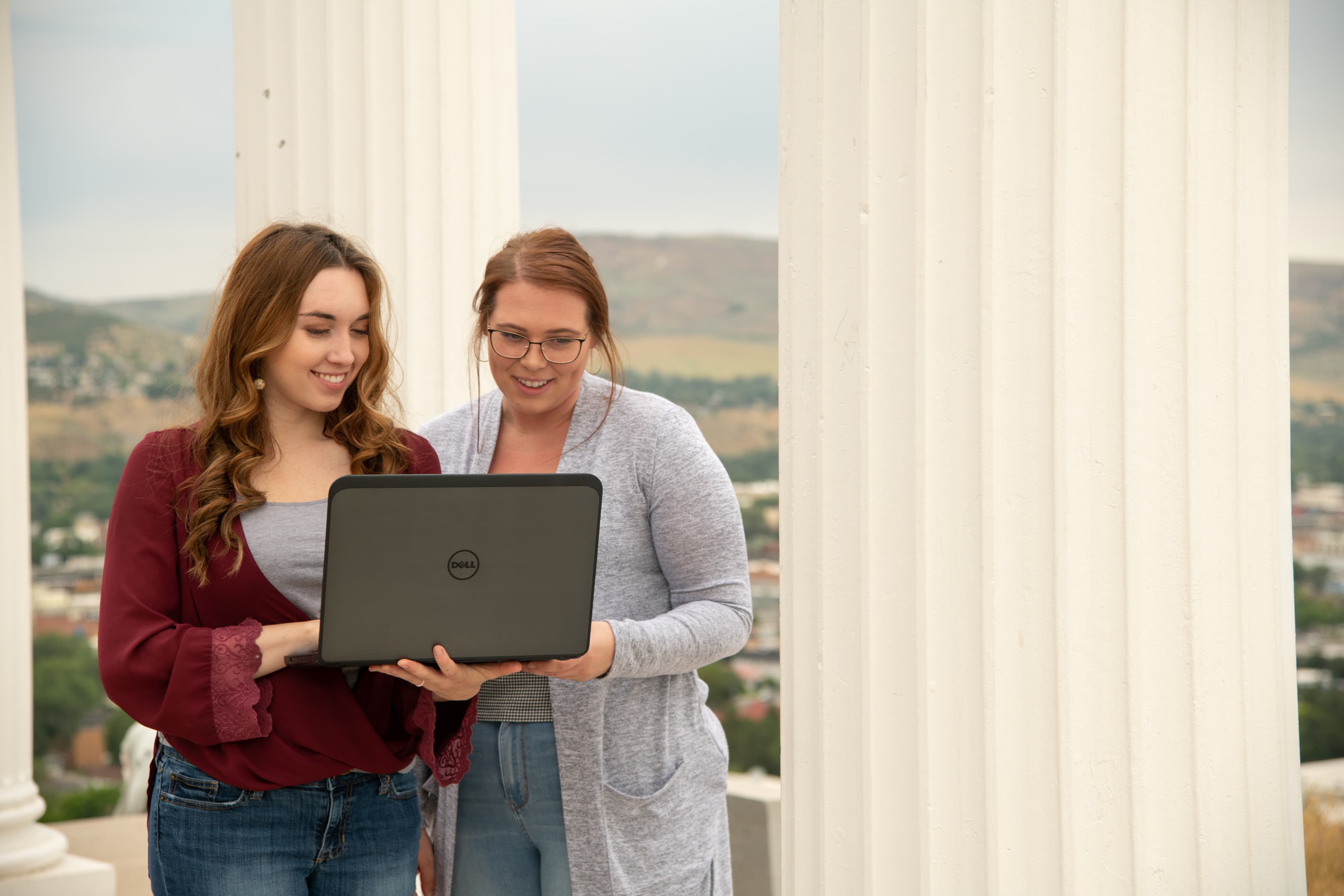 Two students sharing a laptop outdoors.