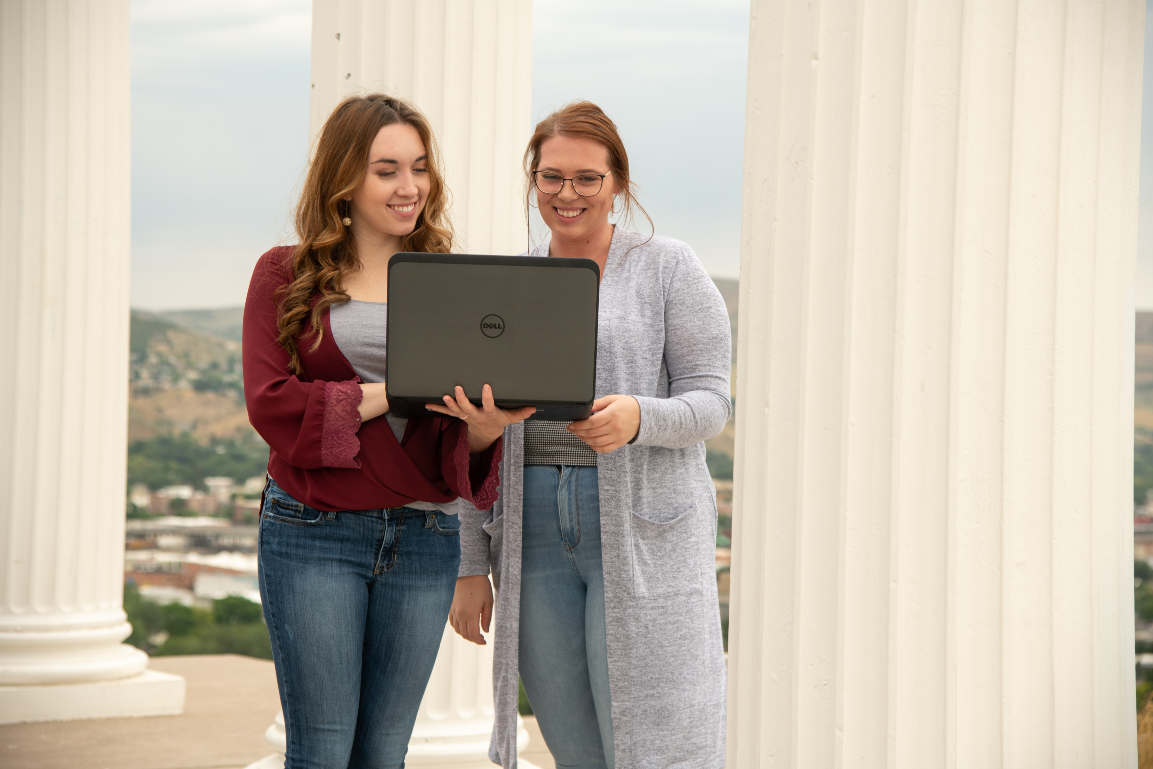 Two students sharing a laptop outdoors in front of pillars on Red Hill.