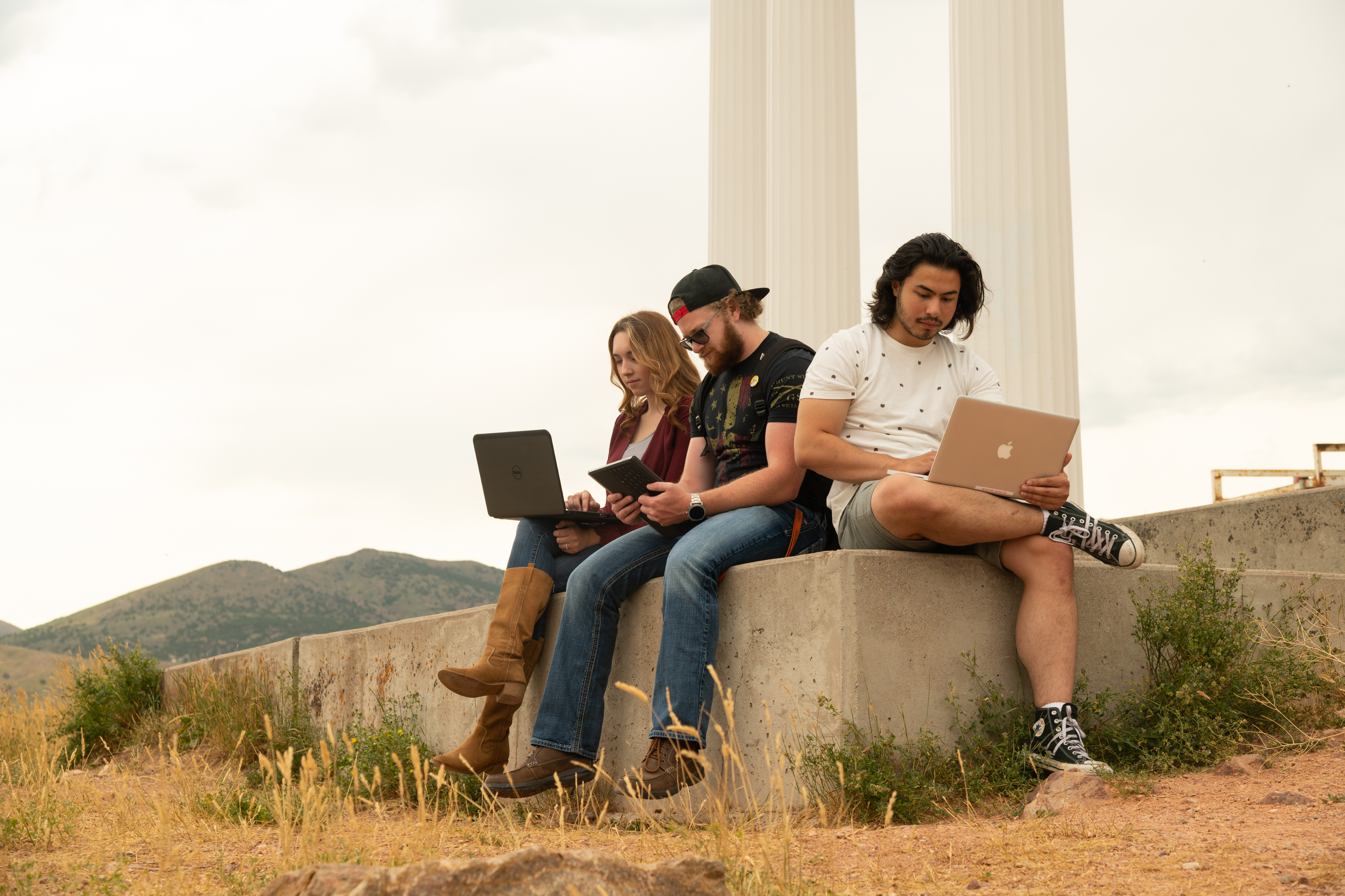 Students sitting under the pillars atop red Hill, using technology.