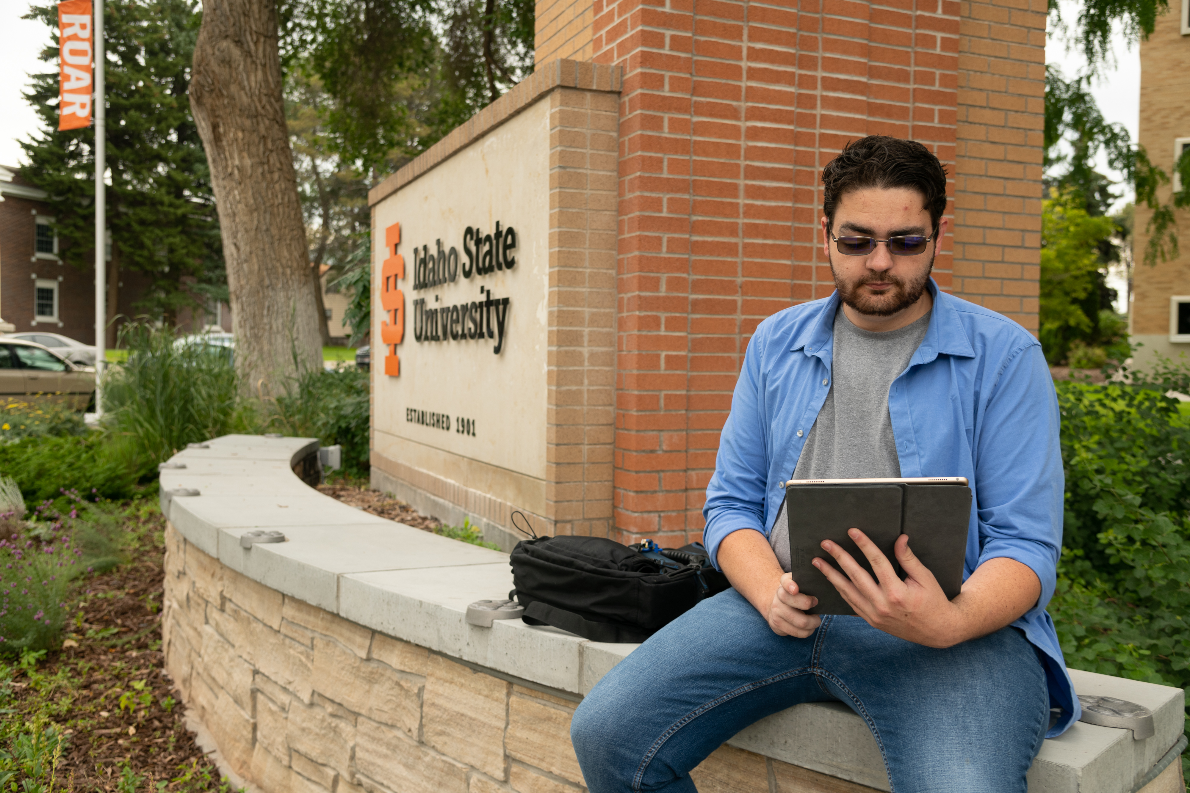 Student using a laptop outdoors next to an ISU logo.