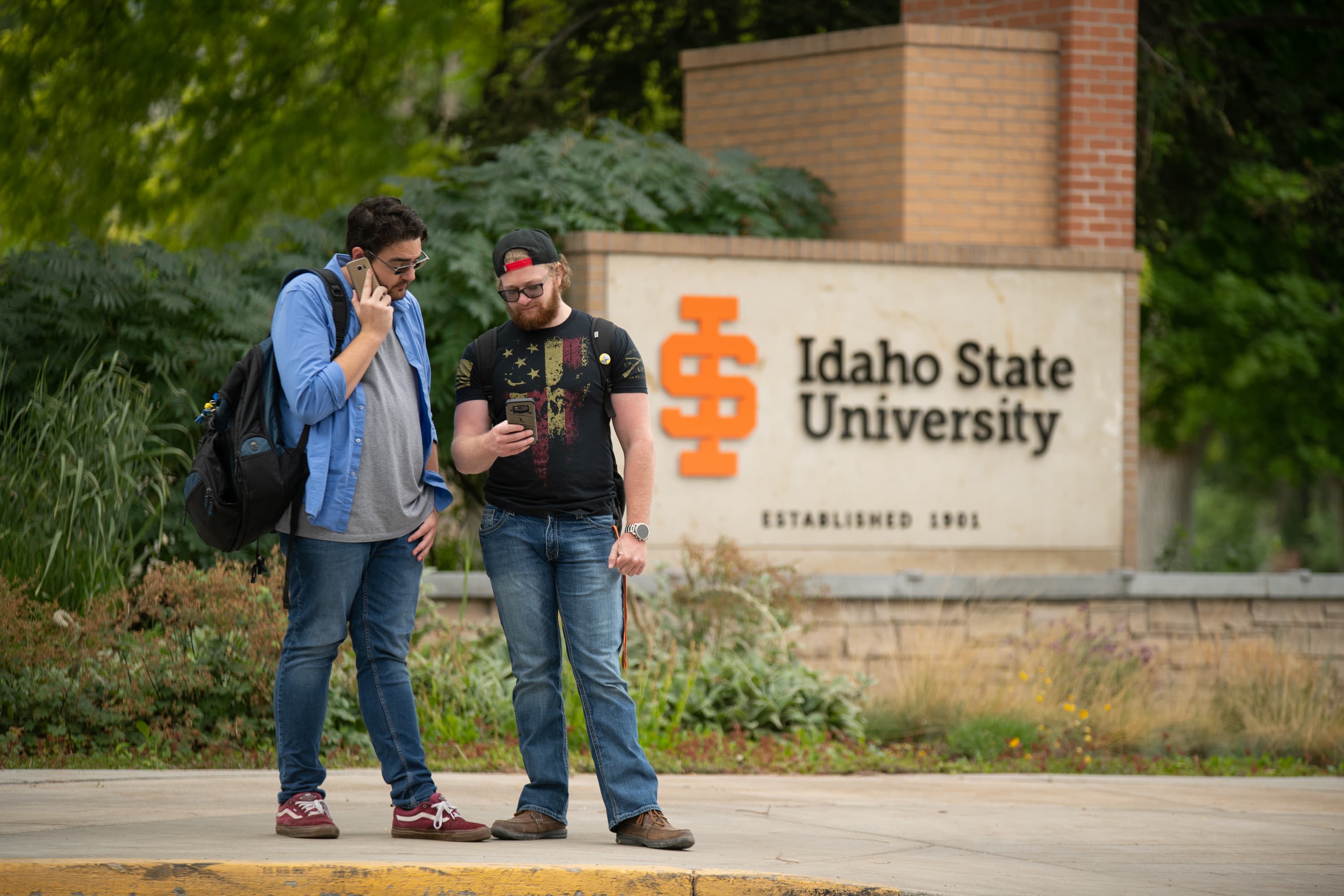 Students looking questioningly at a laptop in front of an outdoor ISU logo.