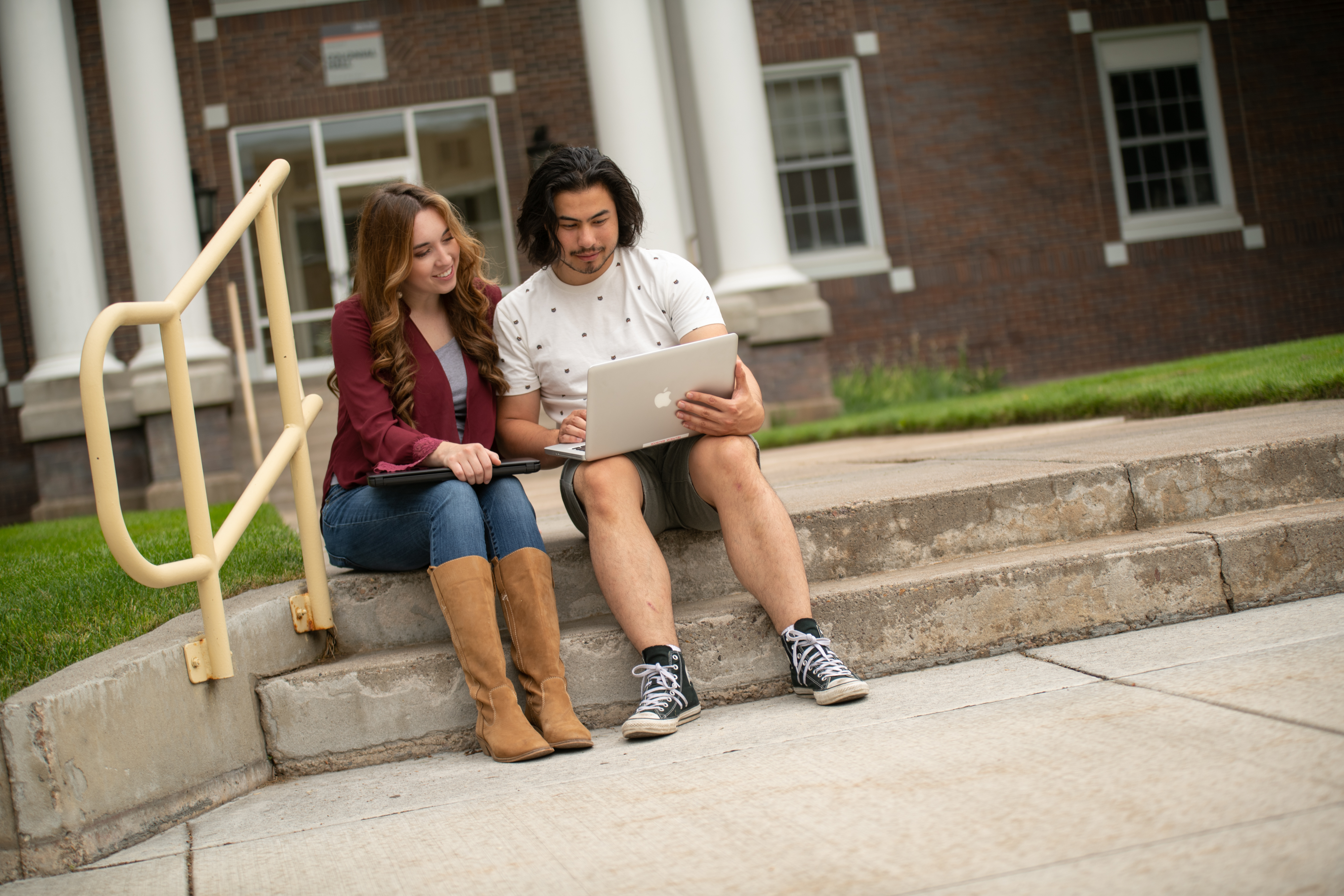 Two students sitting on a pair of steps, looking at one student's laptop.
