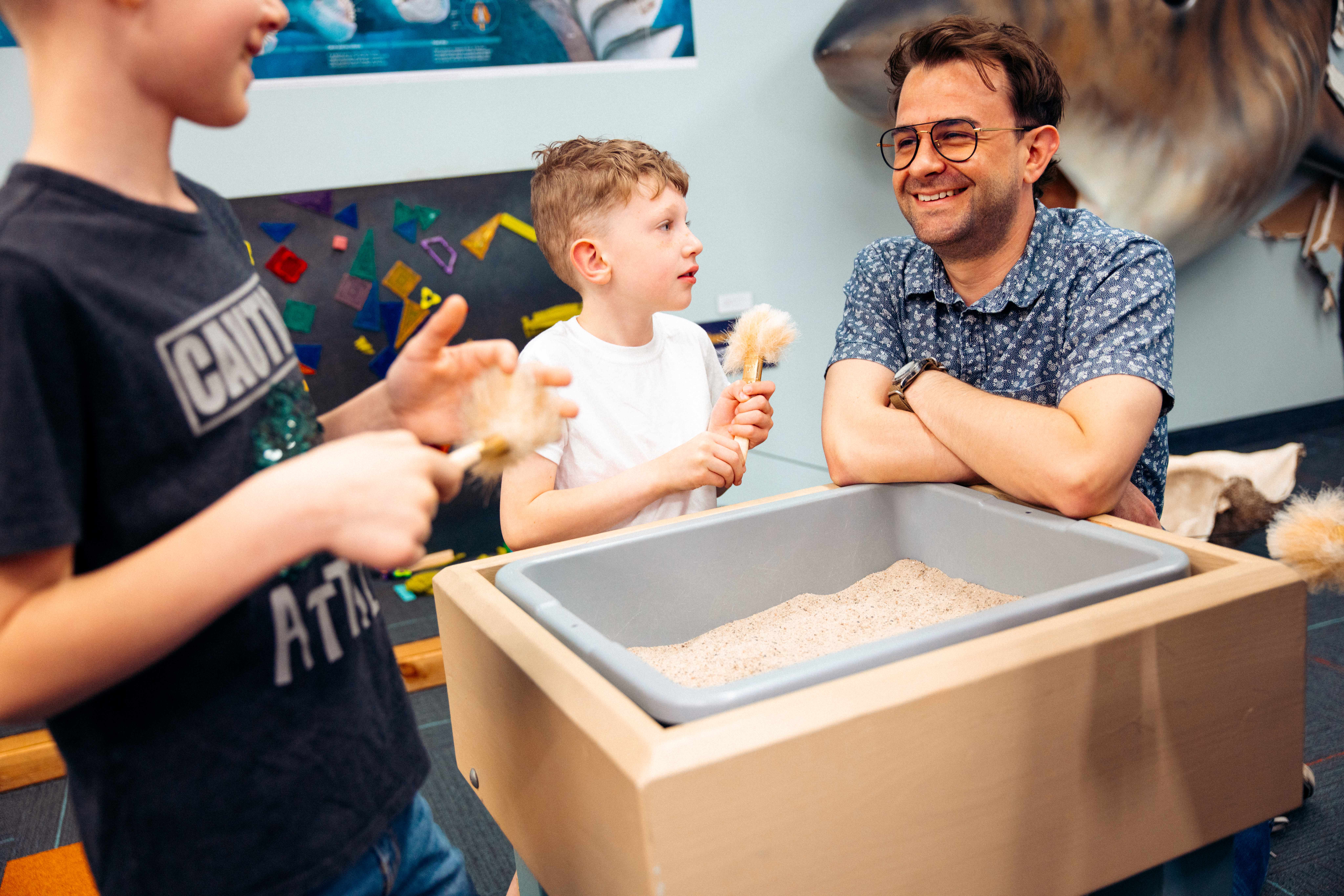 Father and two sons exploring a small fossil excavation box