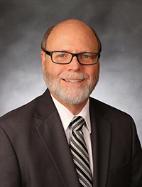 Dean Walter Fitzgerald with black tie and jacket and black framed glasses