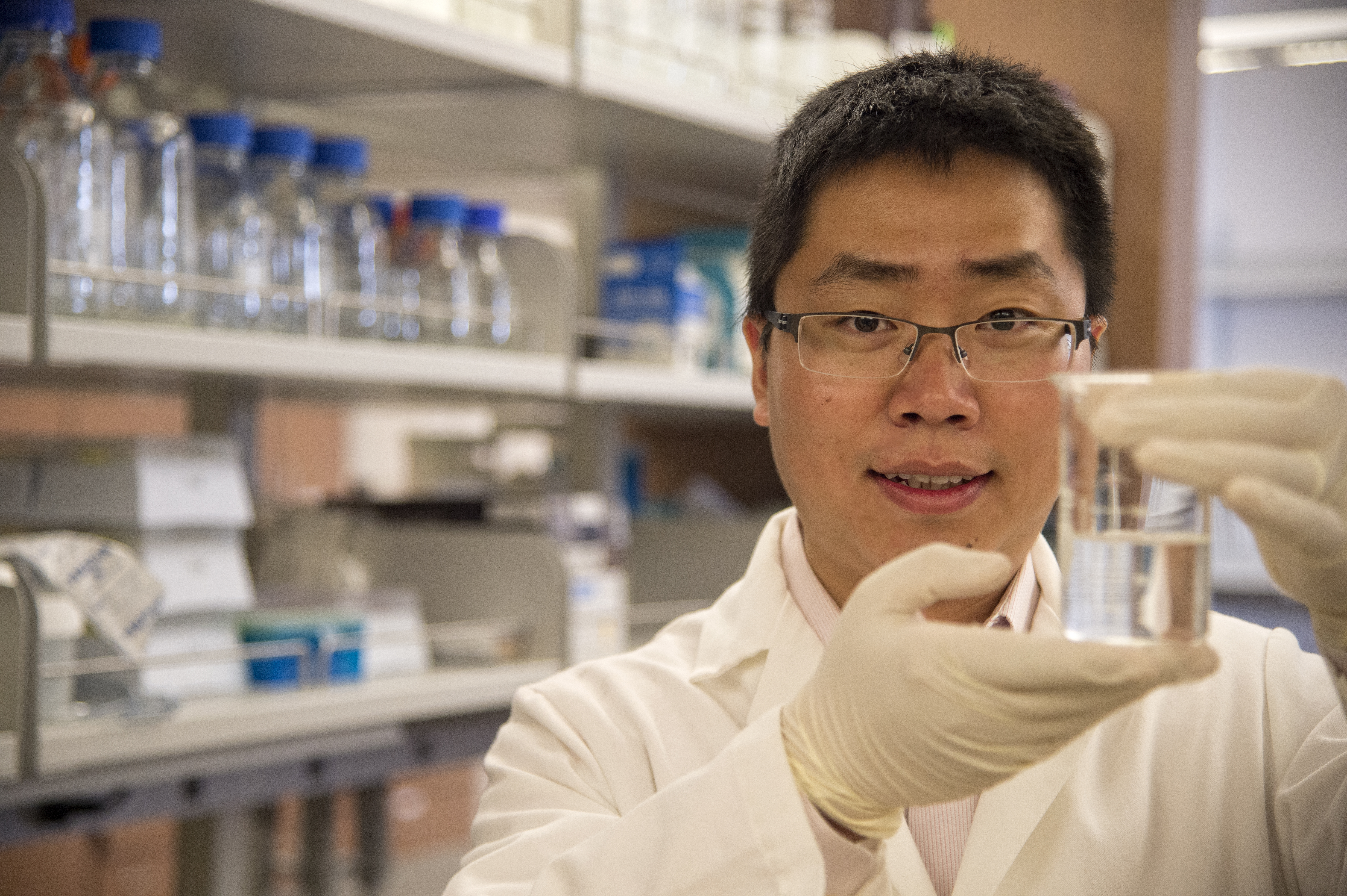Pharmaceutical scientist in white lab coat in his lab with beaker of fluid