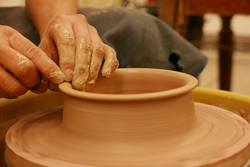 A person's hand shaping clay on a pottery wheel