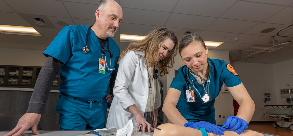 2 students and an instructor practice injections on a sim arm