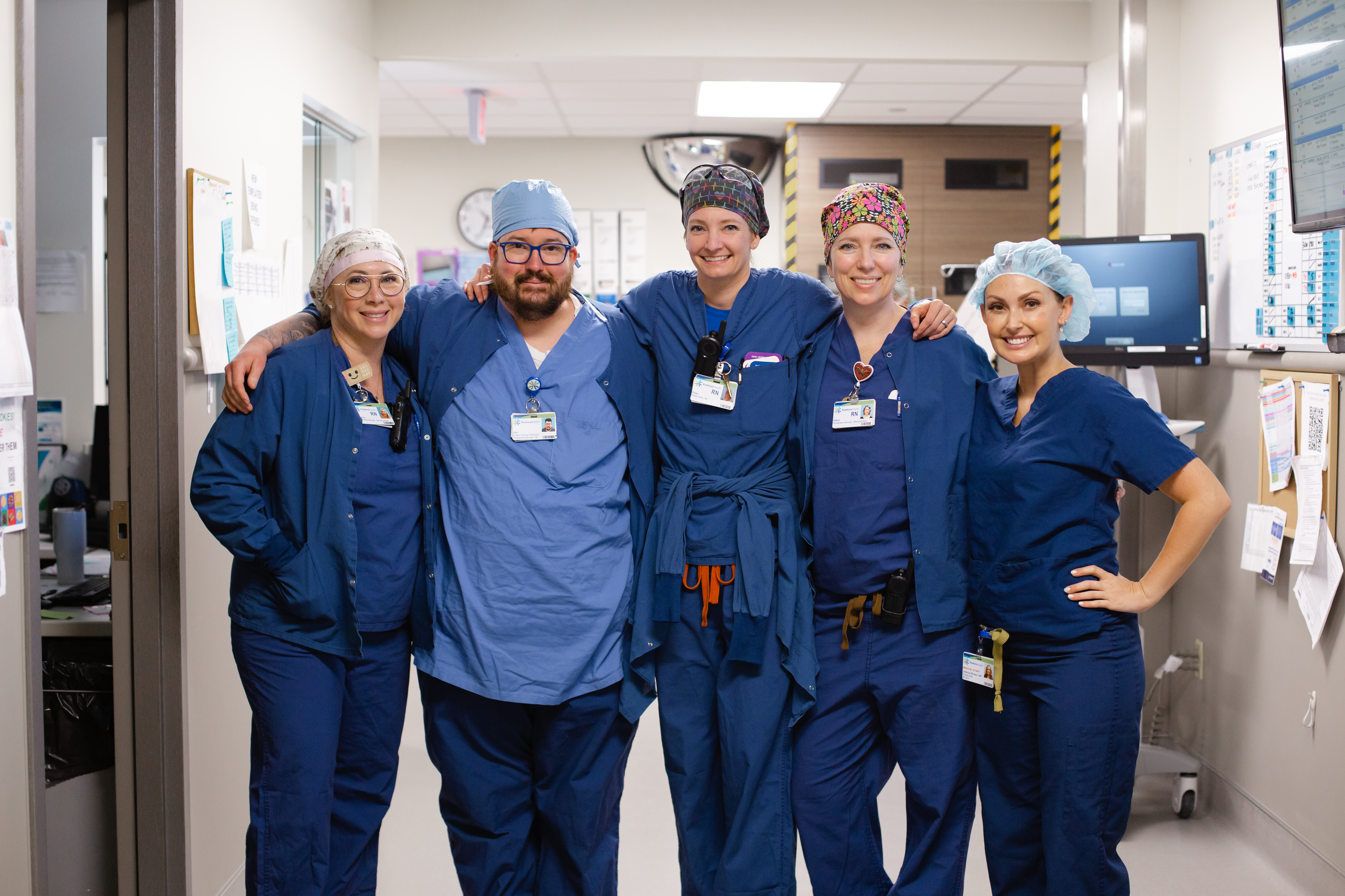 5 nurses in blue scrubs stand together with arms around each other