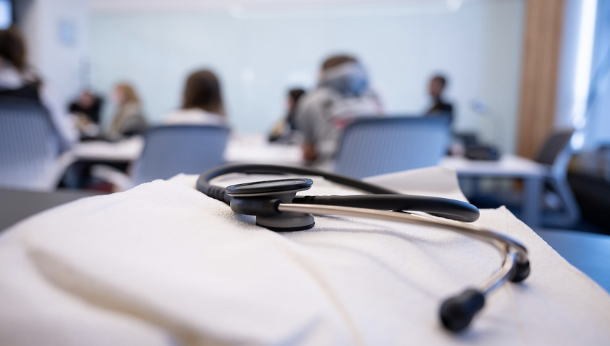 Close up of lab coat and stethoscope with students in lecture