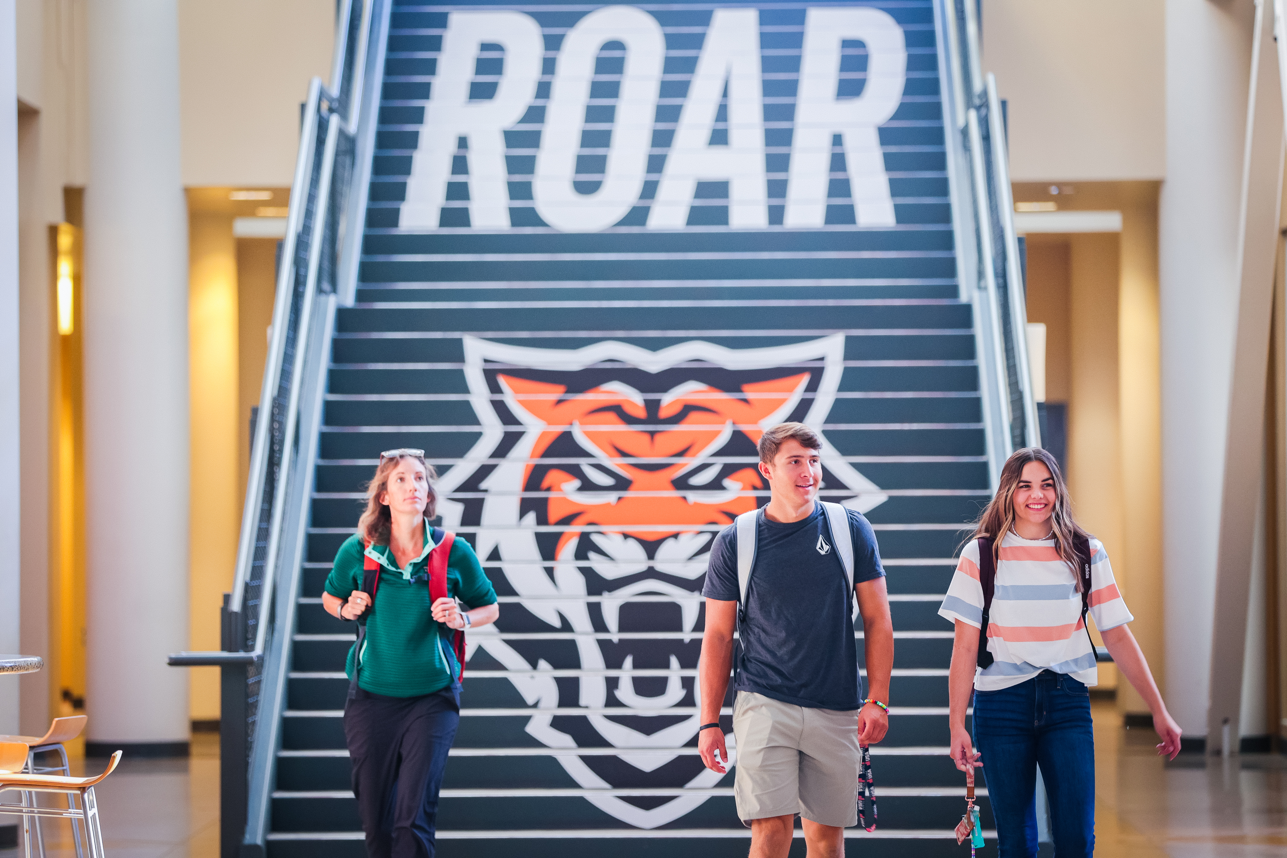 Three students walking in front of a stairway with the ISU Bengal Logo behind