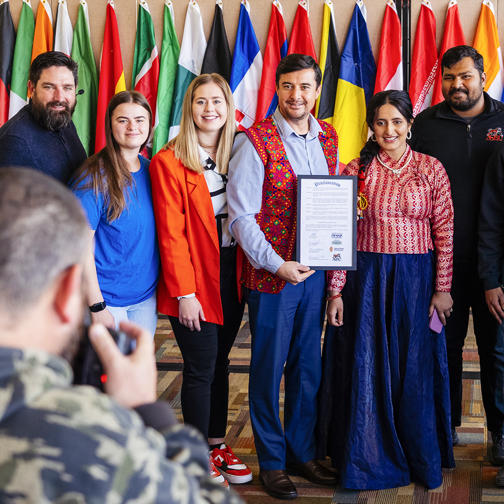 The International Programs Office having their photo taken in front of country flags