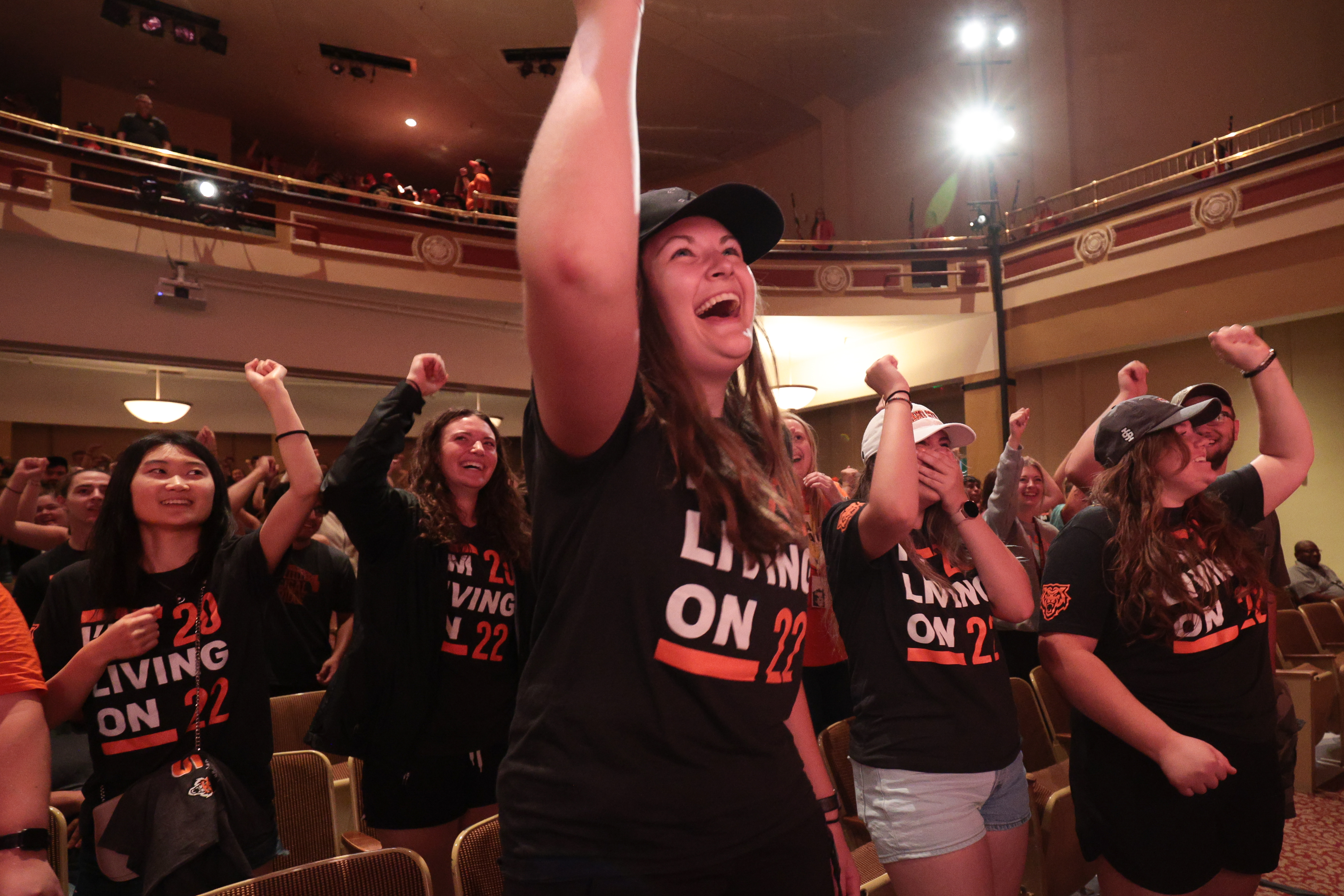 A group of students standing indoors with one arm raised.