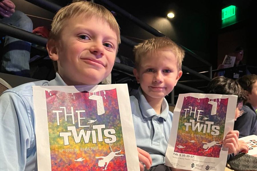 Two 4th graders sit in the Black Box Theatre holding the Twits program and smiling