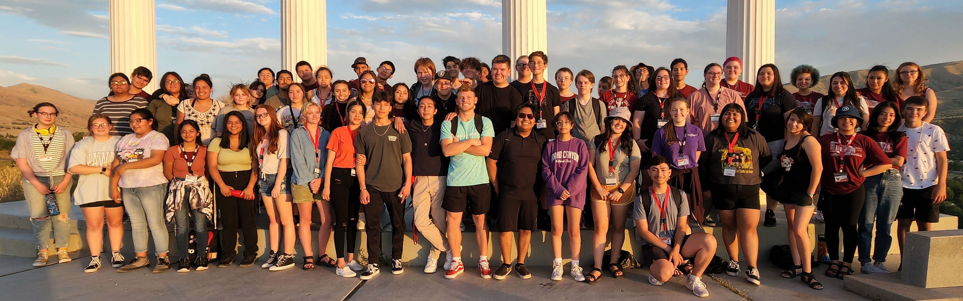 Upward Bound Programs students and mentors standing in front of ISU's pillars near sunset.