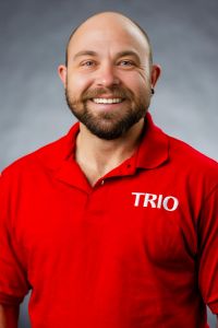 Headshot of Jodi smiling directly at the camera wearing a red TRIO polo on a gray backdrop.