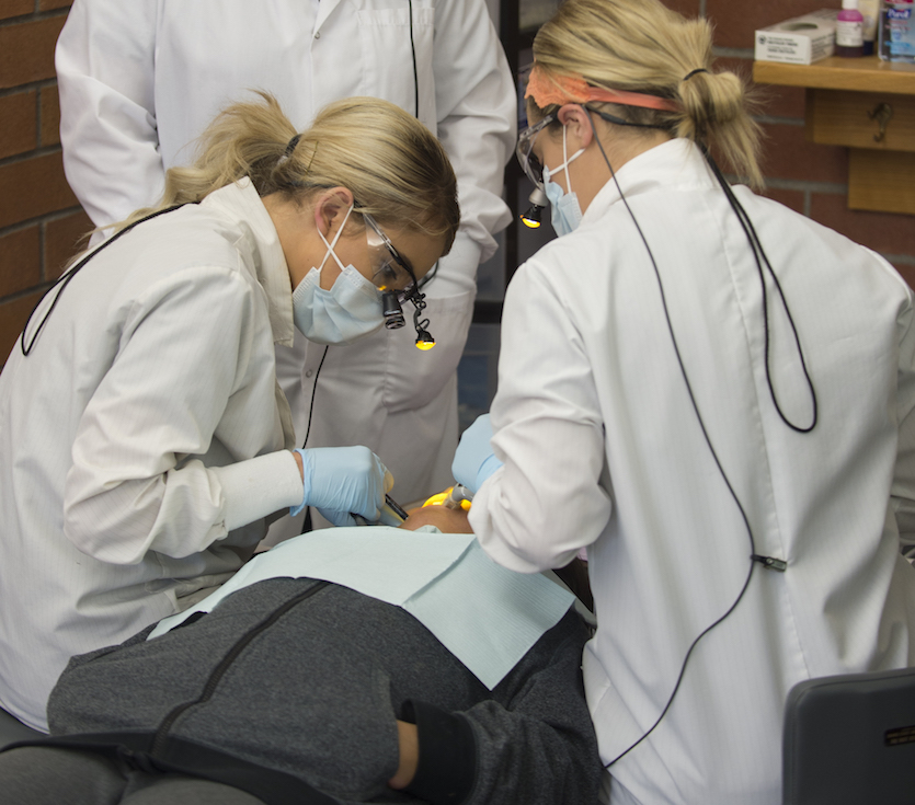 Two dental Hygiene students working on a patient at a clinic. 