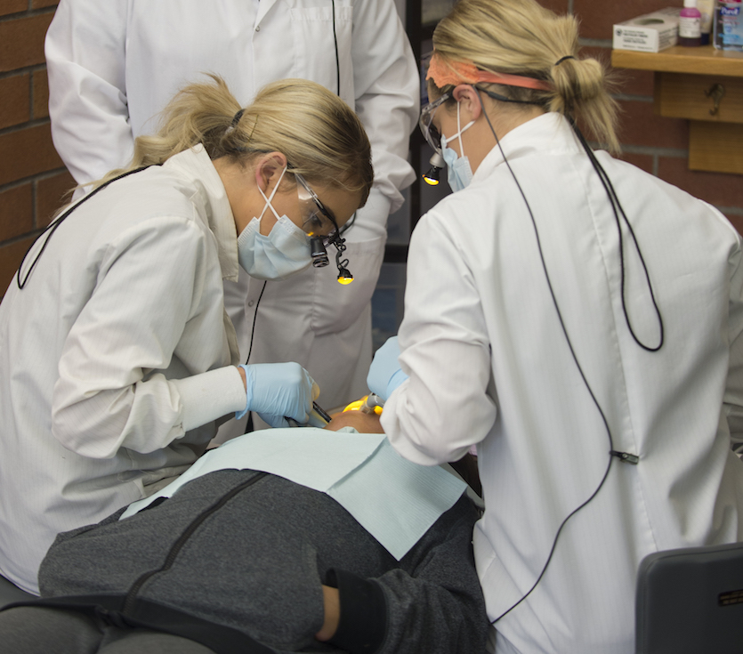 Two dental Hygiene students working on a patient at a clinic.