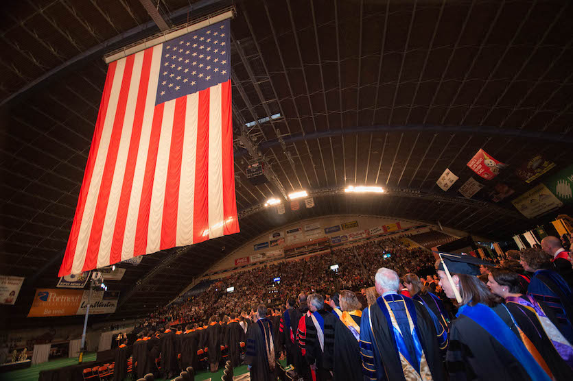 A photo of the large flag at Holt Arena hanging down over commencement participants