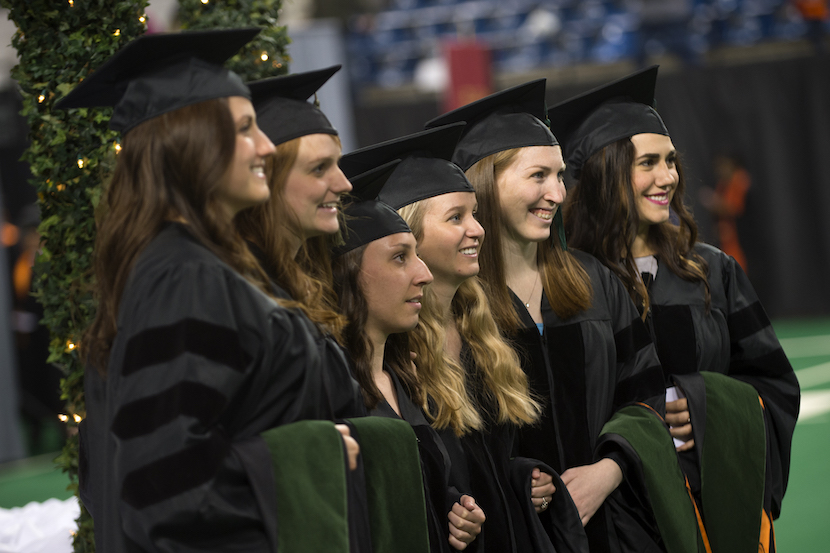 A group of eight students dressed in their robes and caps getting their picture taken at commencement exercises. 