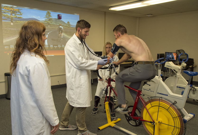 Three students in the Sports Science lab, one of whom is riding a stationary bike and being monitored.