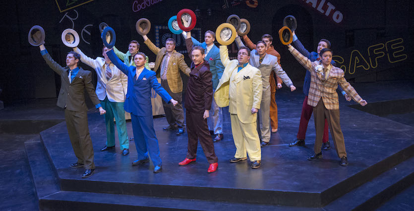 Cast of Guys and Dolls onstage posing with their hats over their heads.
