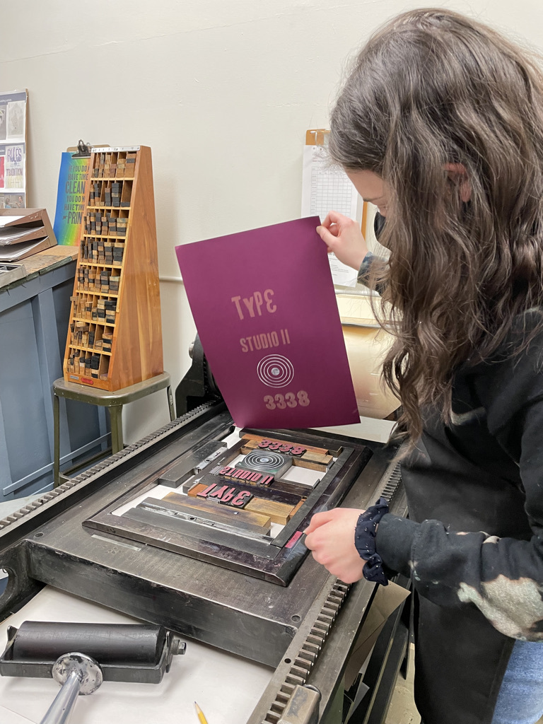A student hand-prints a poster on a Pinyon Jay Press.