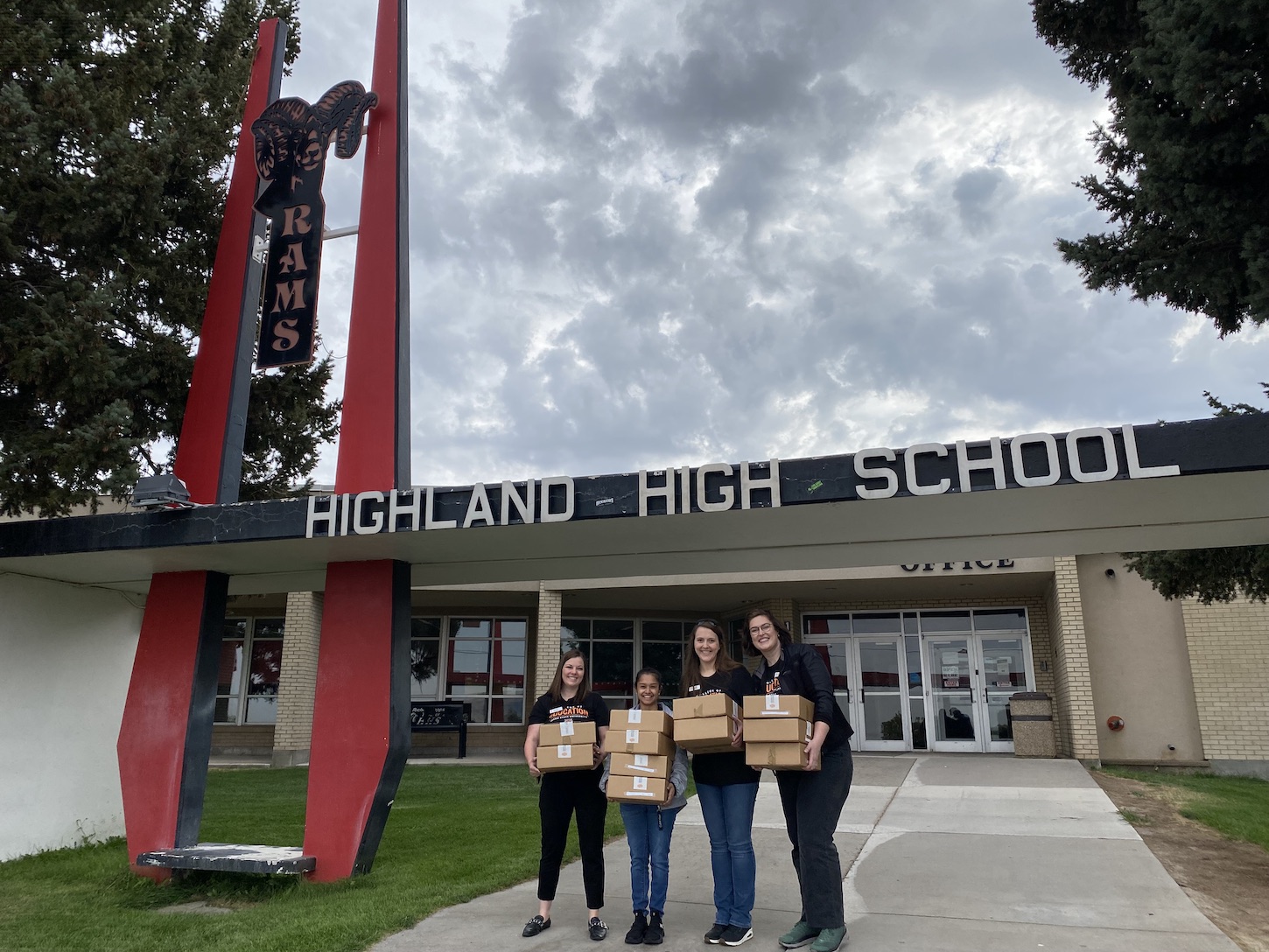 A group of women stand outside a school with boxes.