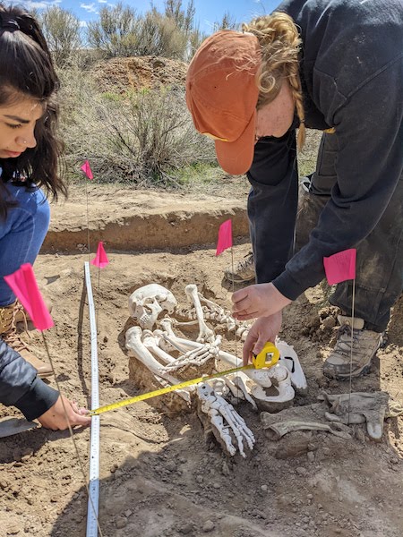 Two students study a skeleton in the ground