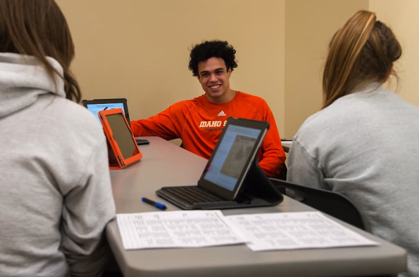 Student-athletes in class sit around a computer