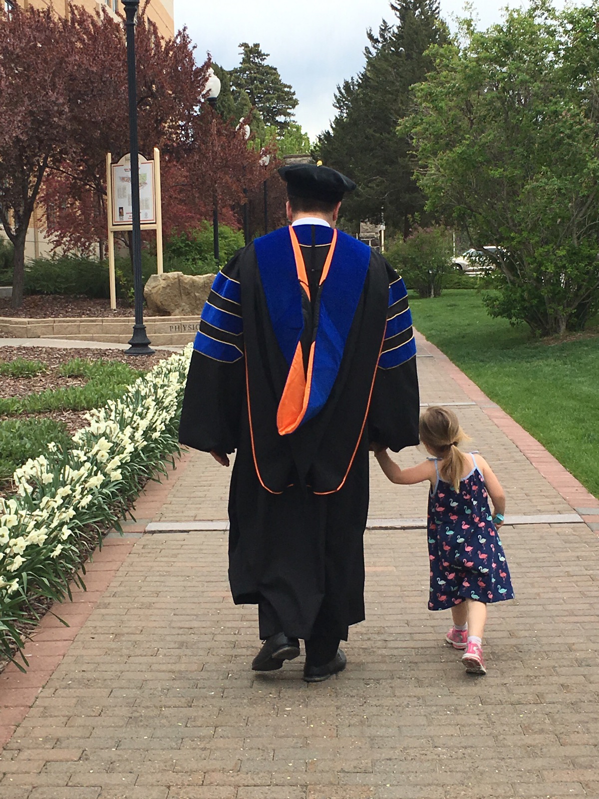 A graduate in regalia walks with a small child.