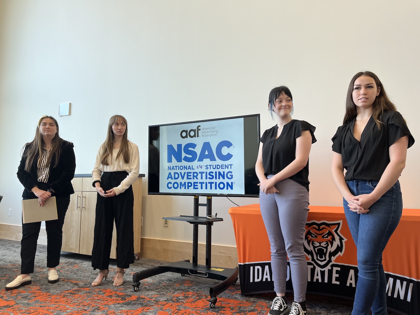 Four women stand next to a computer screen