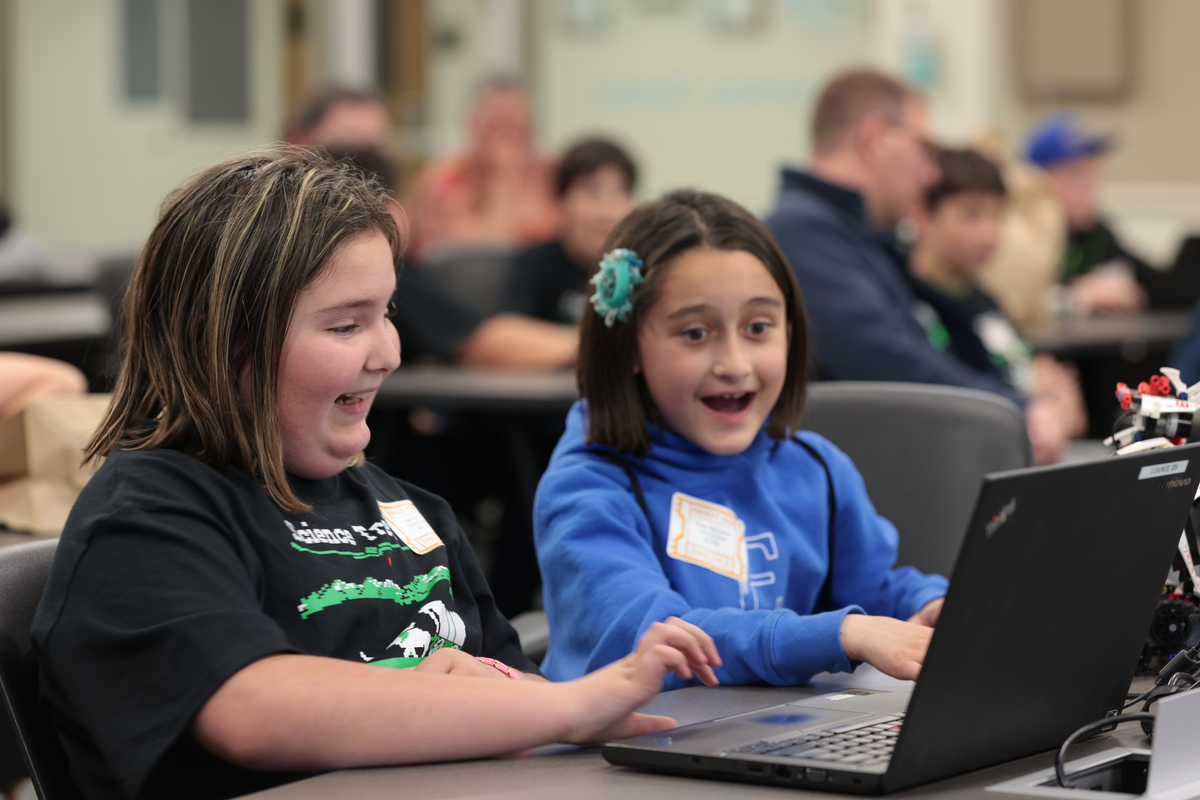 Two young girls smile at a computer