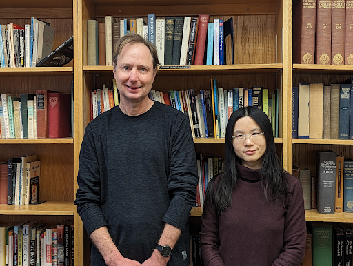 A man and a woman stand in front of a bookcase.