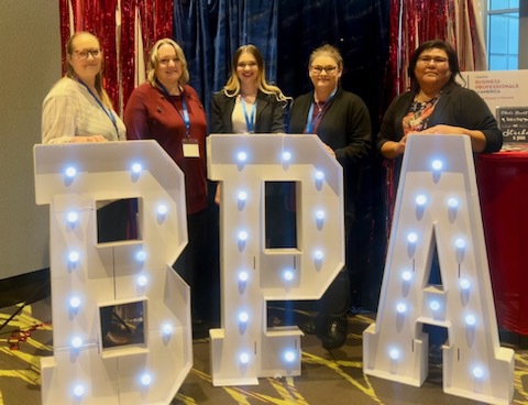 Students at the state regional Business Professionals of American Competition in front of a lighted BPA sign.