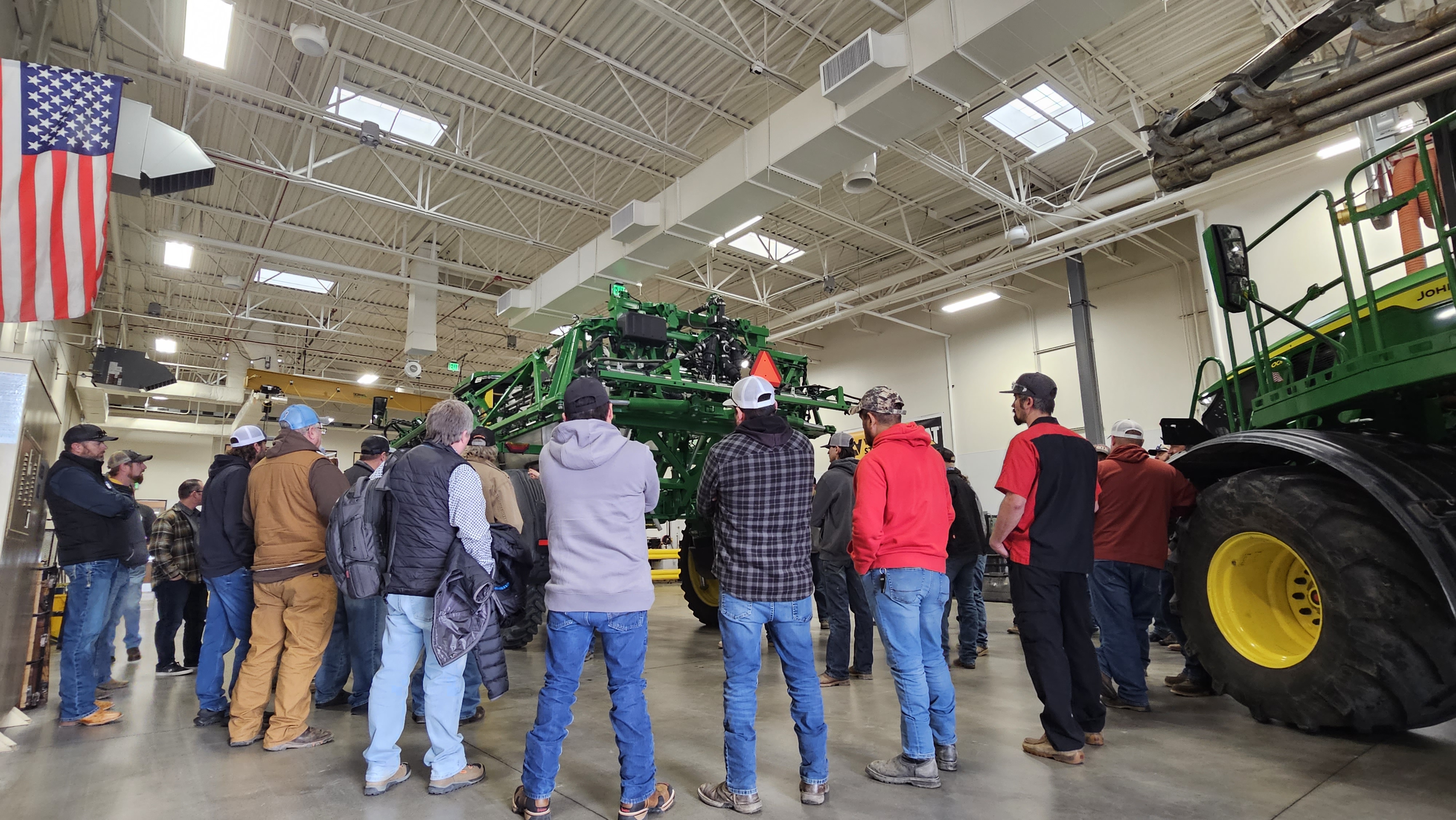 Participants gather around a piece of John Deere farm equipment at an event to certify professionals in the safe use of various agricultural spraying practices for pesticides, herbicides and fertilizers.