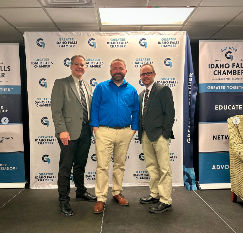Three men stand in front of a backdrop