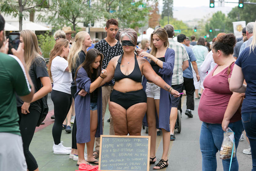 Amy Pence Brown blindfolded and wearing black bikini in a public market.