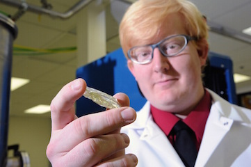 Photo of Eric Burgett in a lab coat examining a crystal in his hand. 