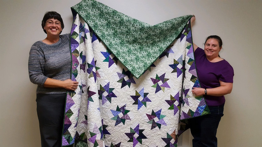 Natosha Holmes, Vendor Coordinator Jody Finnegan, Fair Coordinator, display handmade quilt that will be auctioned.