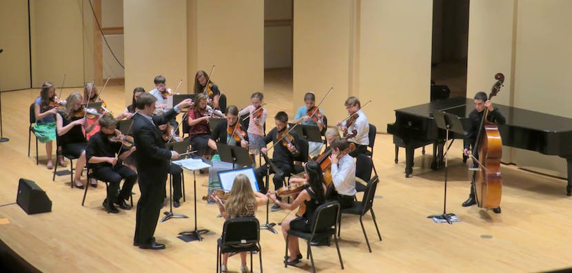 Photo of group of stringed instrument musicians playing on stage at Performing Arts Center.