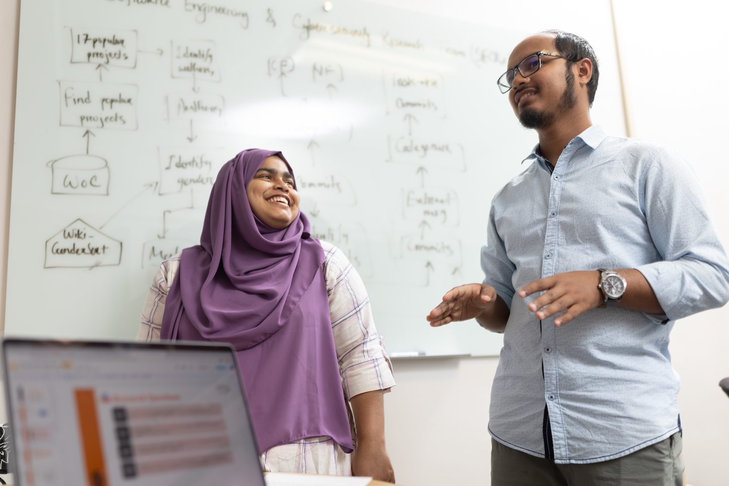 A woman and a man talk near a white board