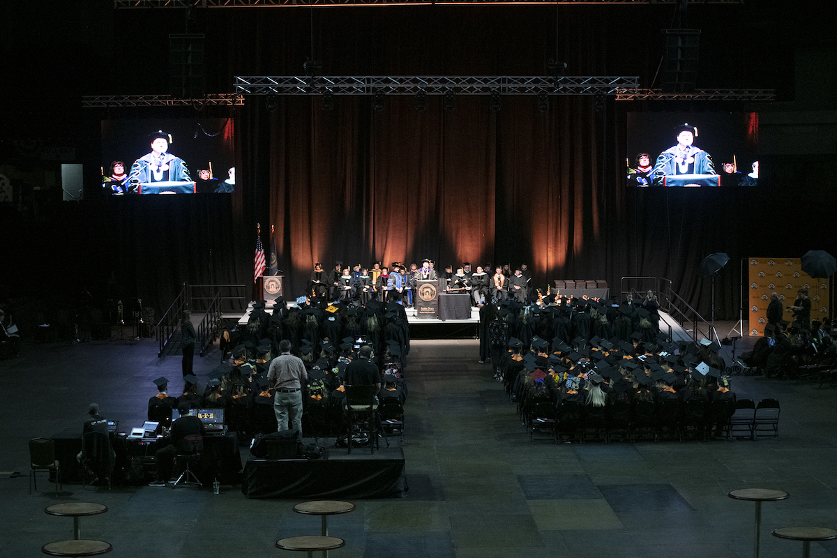 ISU Meridian commencement setup on the floor of the arena, with faculty seated and President Satterlee at the podium.