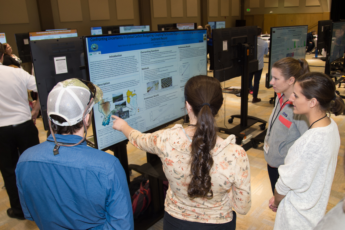 Photo of a student explaining a research poster to two other people at the research symposium.