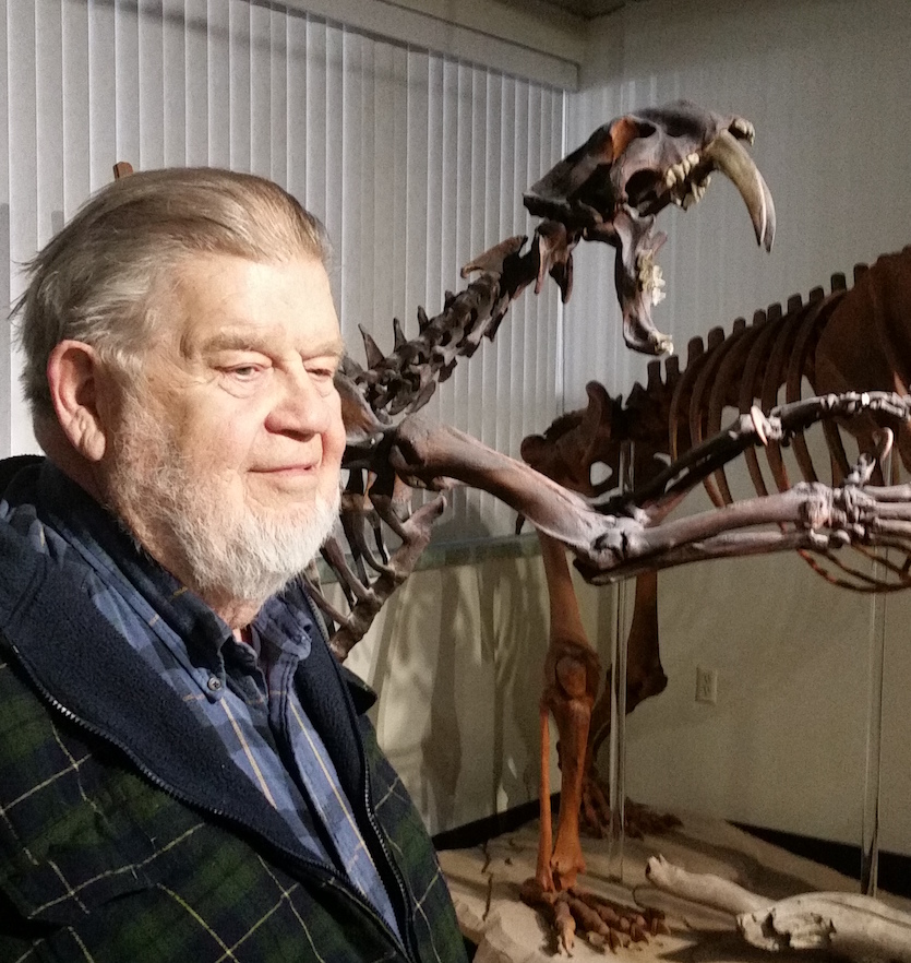 A photo of Bill Akersten with a saber-toothed tiger skeleton in background