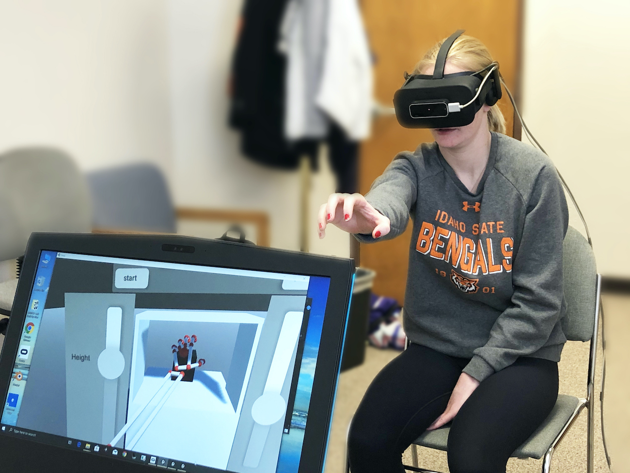 A volunteer, with virtual reality headset on, tests the virtual reality system that is pictured on a computer in the foreground.